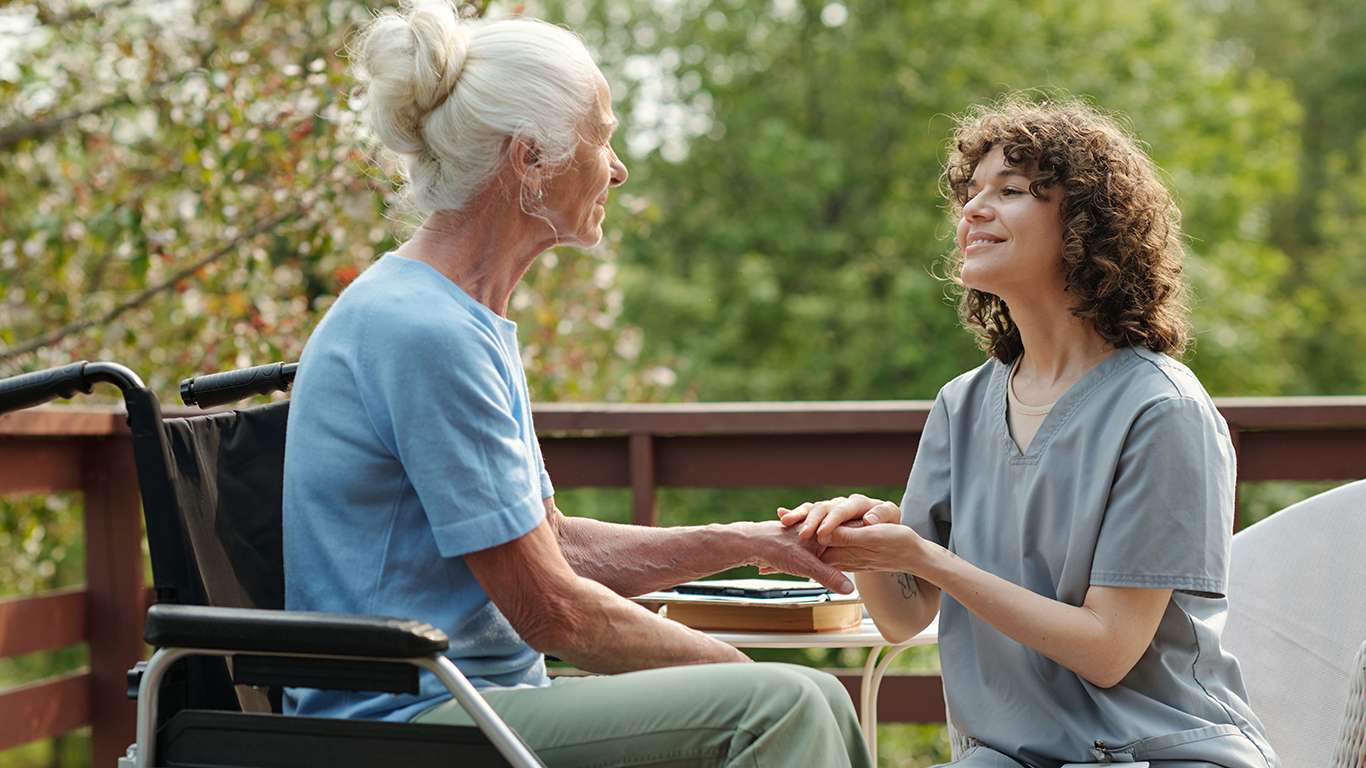 Young smiling caregiver uniform looking elderly woman with disability